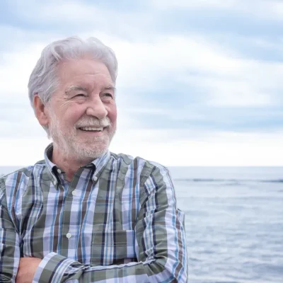 Portrait of old senior man smiling enjoying sea holiday or retirement. Cloudy sky and horizon over water